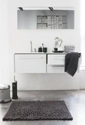 a minimalist neutral bathroom with a floating vanity with storage, a long mirror, grey linens and simple decor