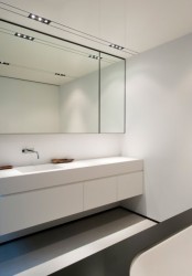 a sleek minimalist black and white bathroom with a statement mirror, a white floating vanity, a white bathtub and built-in lights