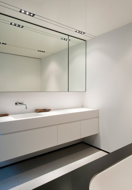 a sleek minimalist black and white bathroom with a statement mirror, a white floating vanity, a white bathtub and built-in lights