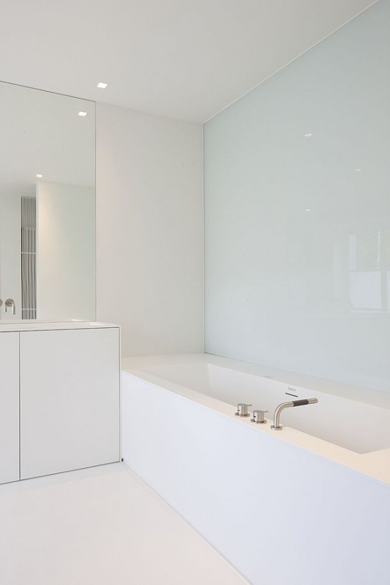 a white sleek minimalist bathroom with a glass wall, a statement mirror, white furniture and appliances