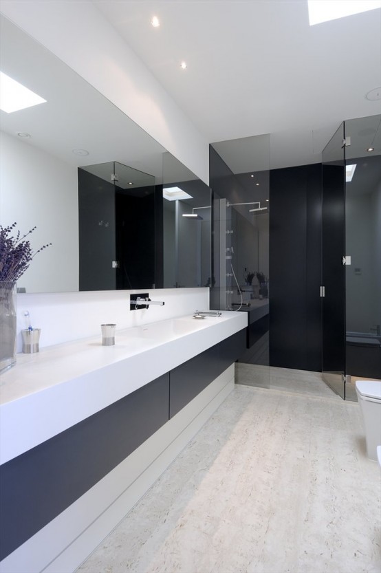 a minimalist contrasting bathroom with a long and sleek vanity in black and white, a statement mirror, a shower clad with dark glass