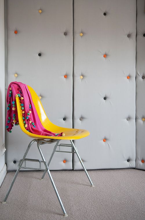 Upholstered grey walls with colorful decorative nails make the space ultra modern and playful