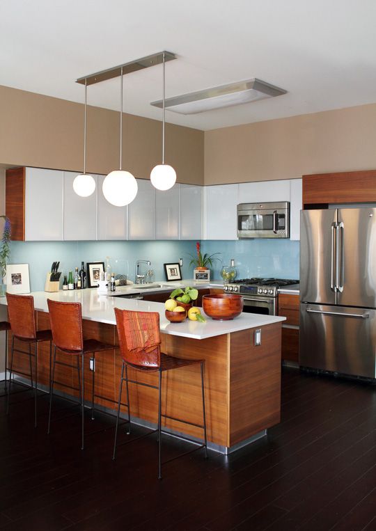 a rich-stained and white mid-century modern kitchen with a blue backsplash, metal appliances, pendant lamps