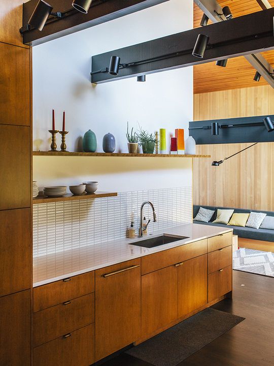 a mid-century modern meets contemporary kitchen with light-colored wooden cabinets, a white tile backsplash, dark beams 