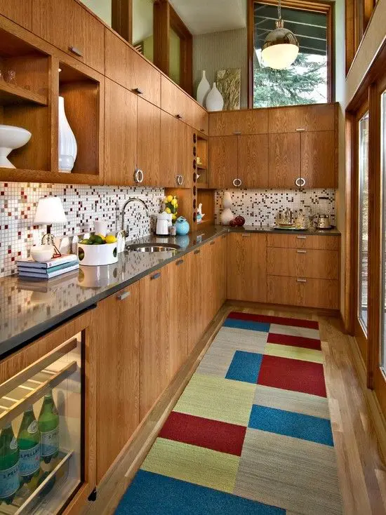 a rich-stained kitchen with a mosaic tile backsplash, a bright color block rug and skylights