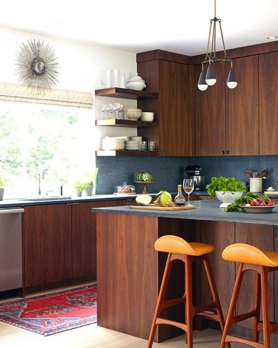 a rich-stained wood mid-century modern kitchen with a grey stone backsplash, orange stools, pendant lamps