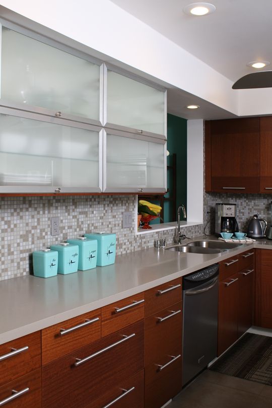 a mid-century modern kitchen with frosted glass and wood cabinets, a neutral countertop and mosaic tile backsplash