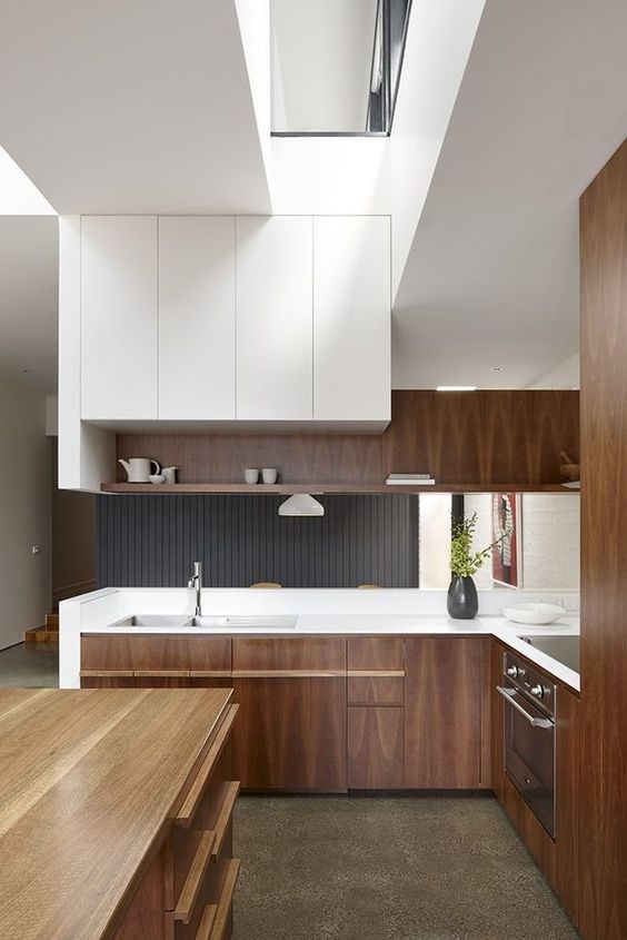 a mid-century modern meets minimalist kitchen with rich-stained and white cabinets, white countertops and a large wooden kitchen island