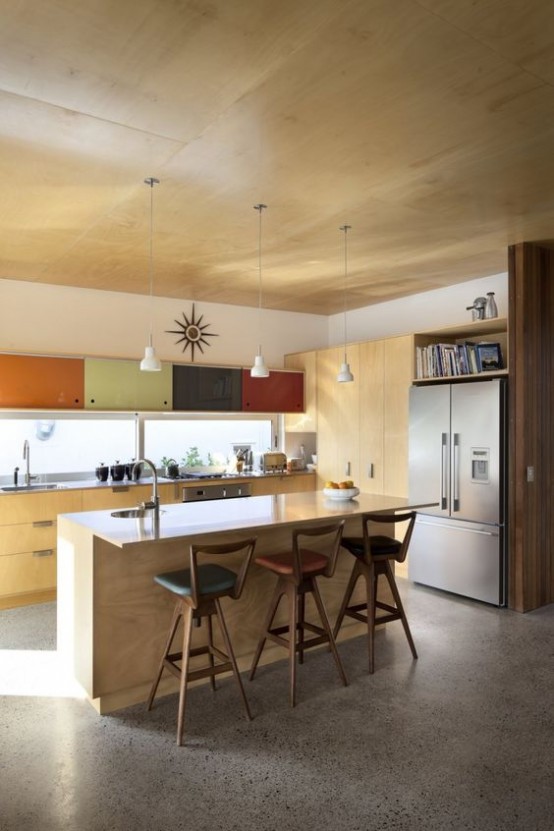 a light colored plywood mid-century modern kitchen with muted colored cabinets, pendant lamps and stools