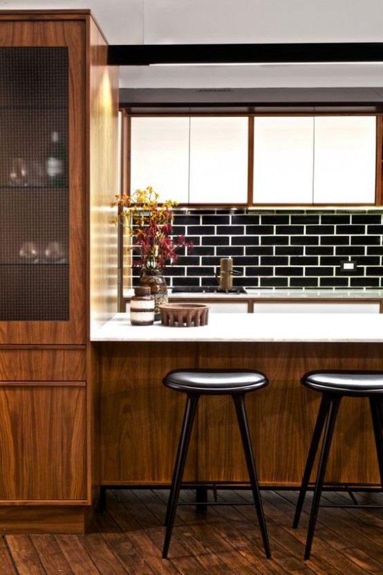 a mid-century modern kitchen with a large wooden kitchen island with a white countertop, black stools, a black tile backsplash