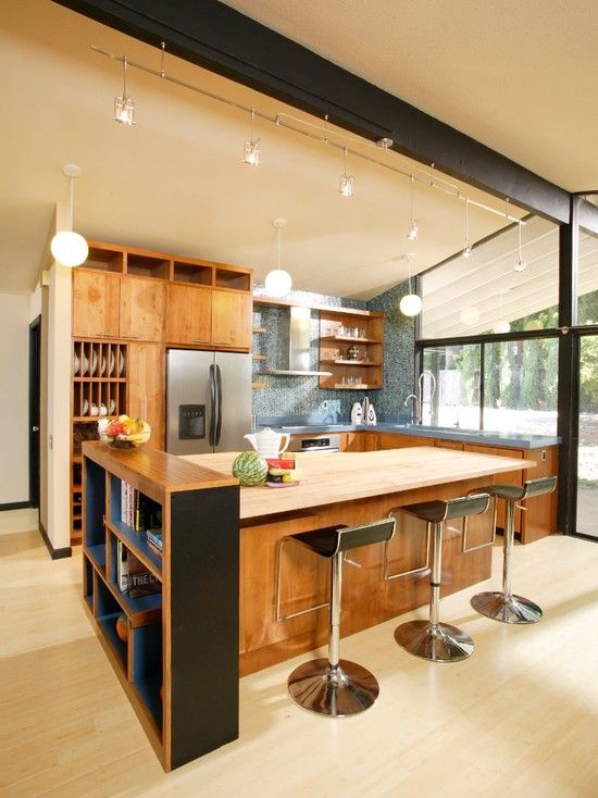 a buttermilk colored mid-century modern kitchen with stained cabinets, a blue tile backsplash, black stools and pendant lamps