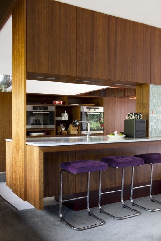 a contemporary meets mid-century modern kitchen with rich-stained cabinets, white countertops and purple upholstered stools