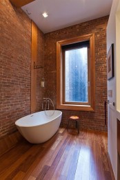 a laconic modern bathroom with brick walls, a laminate floor, a large window and a stool – nothing else is needed here