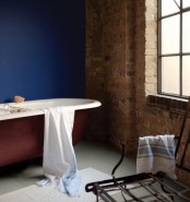 a bold bathroom with red brick walls, a statement blue wall, a red bathtub, a wire chair