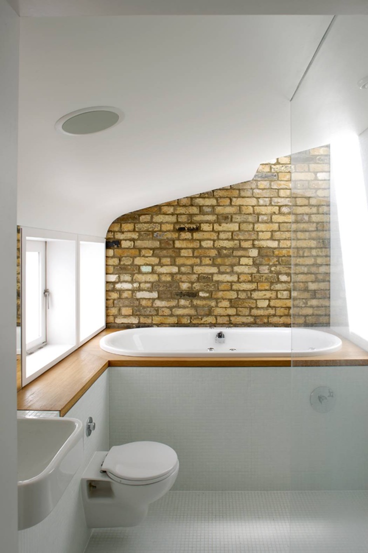 A laconic bathroom with white tiles, a built in bathtub, a brick accent wall, a sink and toilet