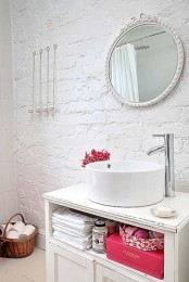 a white bathroom with brick walls, a round mirror, an open vanity, a basket for storage and colorful accents
