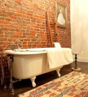 a vintage-inspired bathroom with a red brick wall, a colorful rug, a ladder, a side table and an artwork