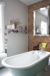 a whimsy bathroom with a brick wall, a pastel green tub, a vintage-inspired mirror and some modern stuff