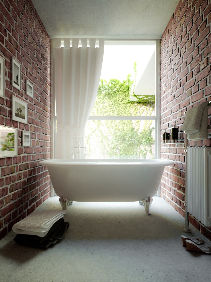 A gorgeous small bathroom with red brick walls, a glazed wall, a vintage inspired tub and a gallery wall