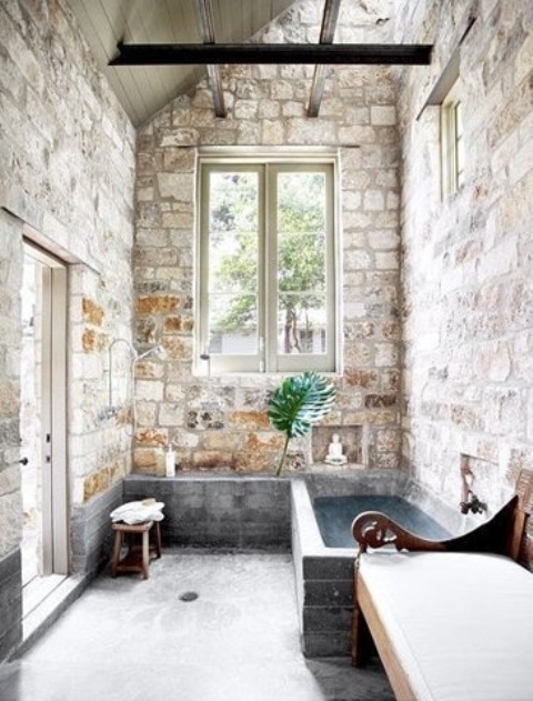 An indoor outdoor bathroom with brick walls, a stone tub, a carved wooden bench, windows and a door