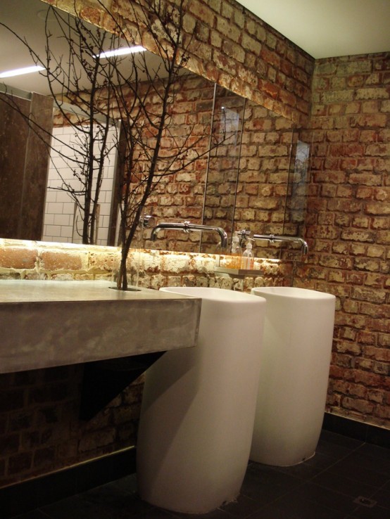 a coontemporary powder room done with a red brick wall, a concrete vanity, free-standing sinks and an oversized mirror