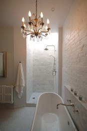 a neutral bathroom with white brick walls, a vintage tub, a crystal chandelier, a shower space also done with bricks