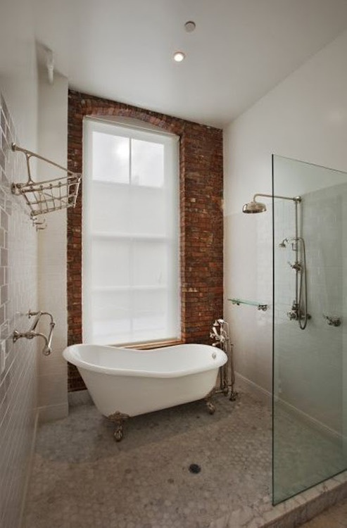 an eclectic bathroom with a brick wall, white subway and marble tiles, a shower space and a vintage tub