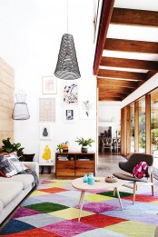 a modern colorful living room with a bold geometric print rug, a neutral sofa, chairs and coffee tables, a bright gallery wall and pendant lamps