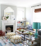 a vivacious living room with a faux fireplace, a grey low sofa, several coffee tables, a bright geometric rug and pretty geometric poufs
