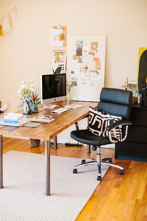 A pretty home office with an industrial desk of wood and metal, a black leather chair, some memo boards and a tassel garland