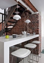 an exposed red brick wall in the eating space brings texture, interest and contrasts the sleek white furniture
