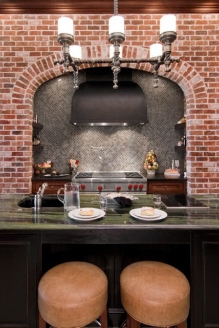 a red brick wall contrasts the grey tiles and a green stone countertop and add colro to the space