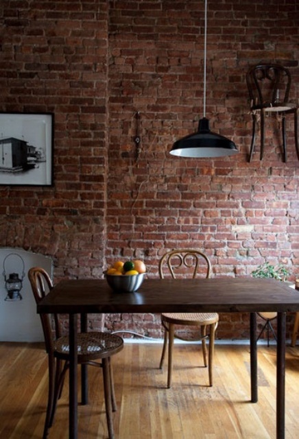 an exposed red brick wall and dark stained wooden furniture for a bold and chic dining space with an industrial feel