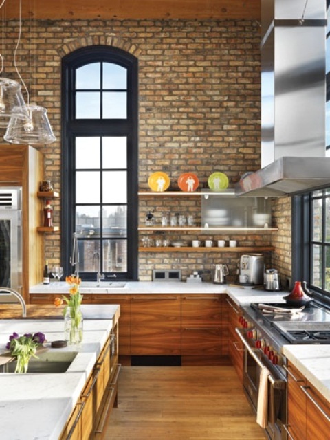 neutral exposed brick walls paired with amber wooden cabinets for a chic and bright kitchen with double height ceilings