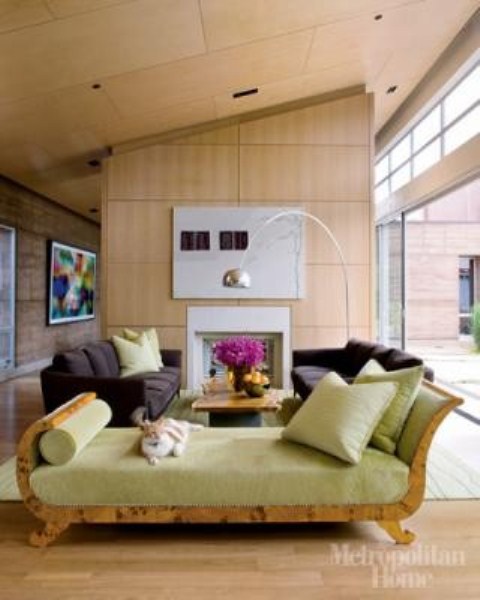 A bright mid century modern living room with plywood walls and ceiling, dark furniture and a green couch with lots of pillows