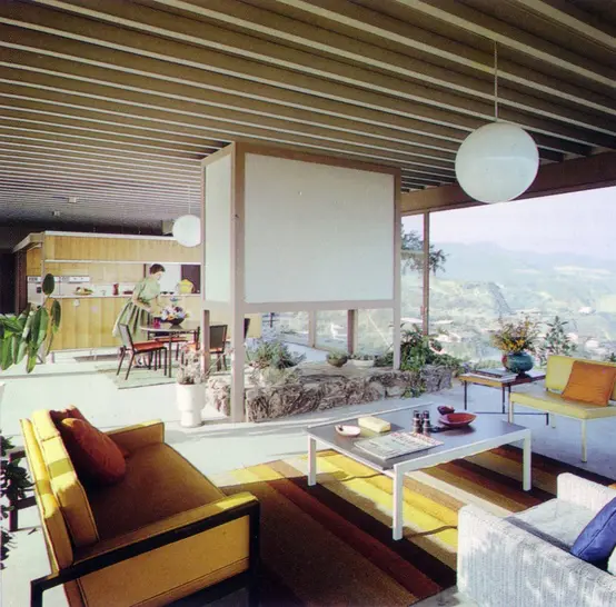 A neutral mid century modern living room with yellow furniture, lots of greenery and a large panoramic view