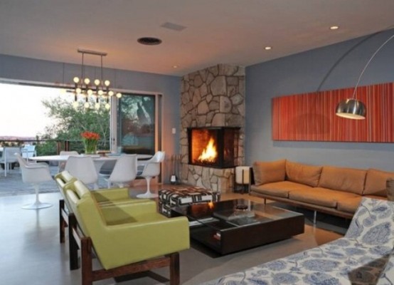 a welcoming mid-century modern living room with green chairs, bright artworks, a built-in fireplace and lots of lamps