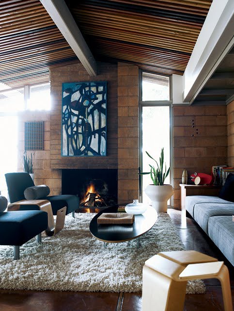 A mid century modern living room with large bricks, navy and grey furniture, a fireplace and an abstract artwork