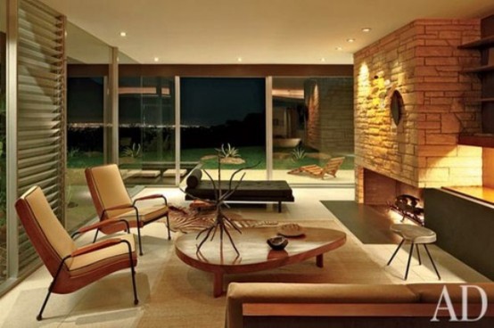 a cozy mid-century modern living room with a fireplace clad with faux stone, stylish furniture and a view
