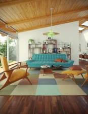 a bright living room with a blue sofa, a colorful plaid rug, bright chairs and lamps and a cool wall unit