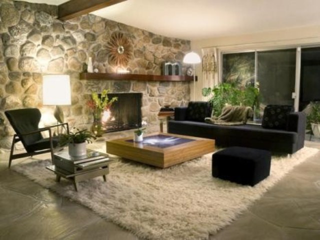 A monochromatic living room with dark furniture, a fluffy rug, a faux stone wall and a built in fireplace
