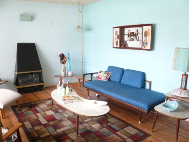 A quirky mid century modern space with a blue couch, a printed rug, a heart and some unusual lamps