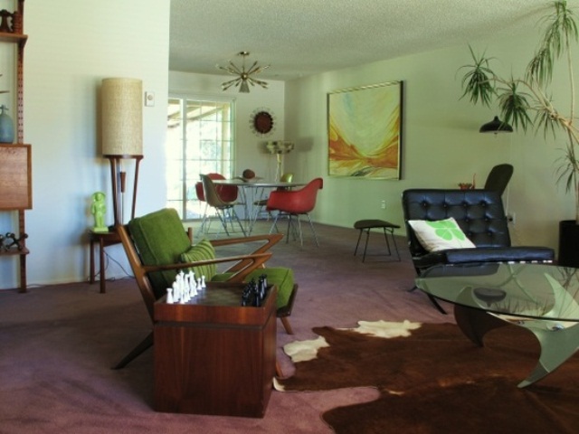 A pastel grene mid century modern living room with dark stained furniture, potted greenery, artworks and lamps