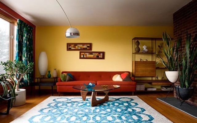 A colorful mid century modern living room with a yellow and brick wall, printed textiles and potted plants