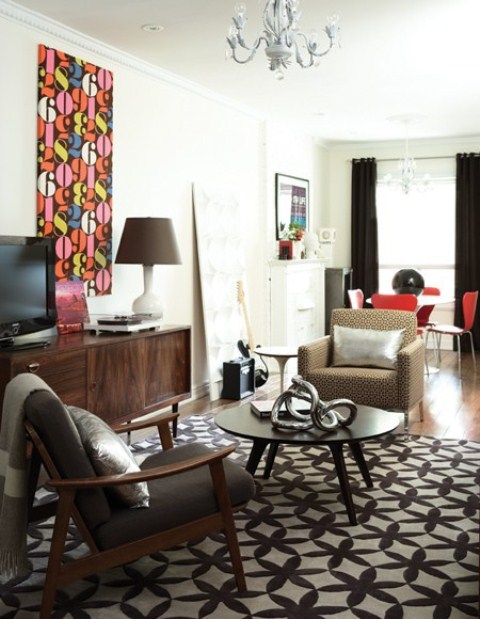 a monochromatic living room done with touches of red and prints, with dark stained furniture and a chic chandelier