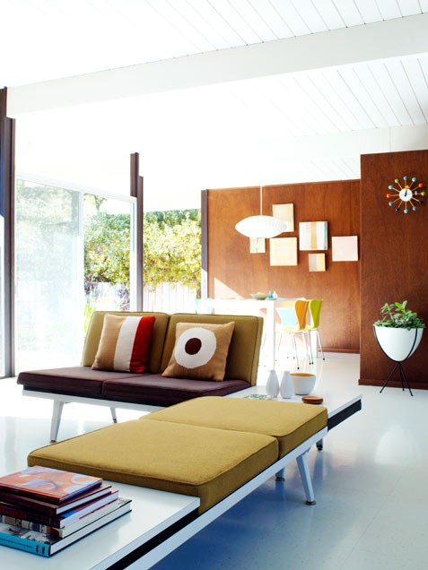 a bright living room with plywood walls, a mustard couch, lots of natural light and a gallery wall
