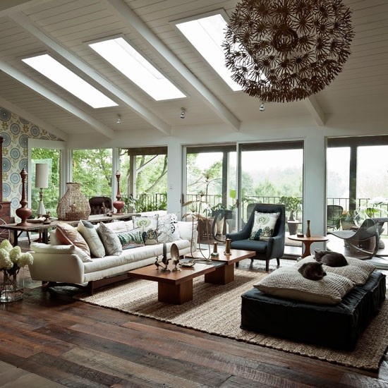 A cozy boho meets mid century modern living room with dark and neutral furniture, skylights, wooden tables and much natural light