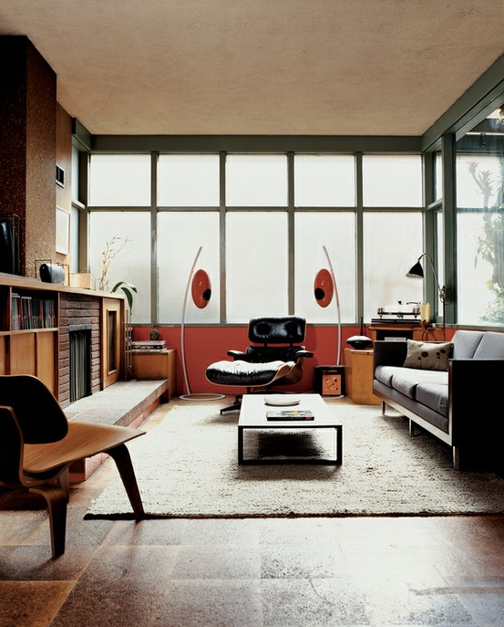 A mid century modern living room with bright orange and yellow touches, dark touches, faux brick, plywood and cork touches