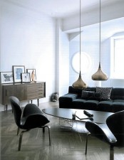 a monochromatic living room with suspended lamps, dark furniture, wood clad floor and a round window
