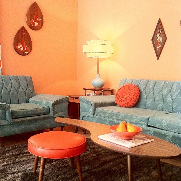A creatively shaped rich stained mid century modern coffee table paired with a coral leather stool looks cool and catchy